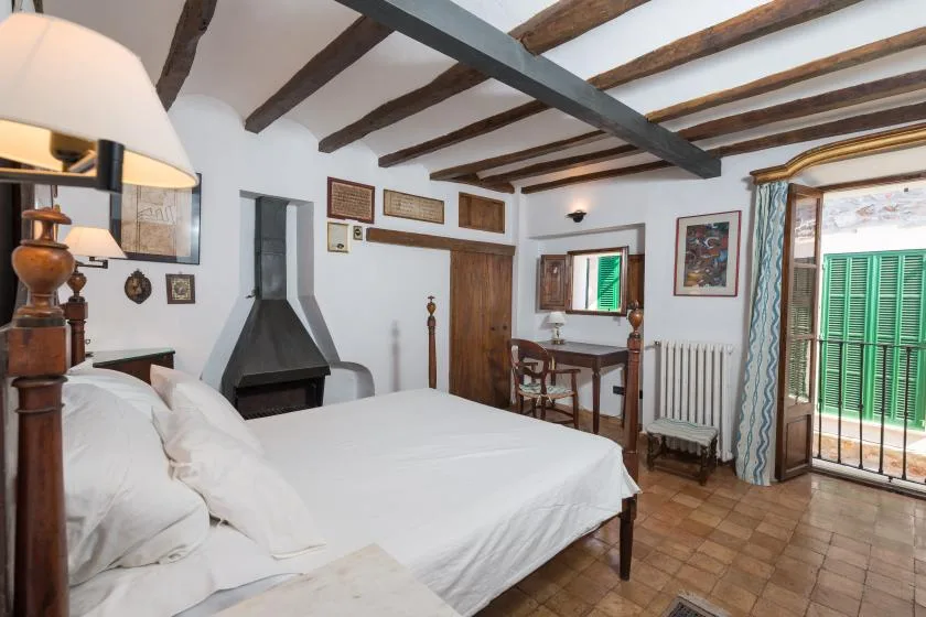 A bedroom with a large bed, fireplace, and exposed ceiling beams.