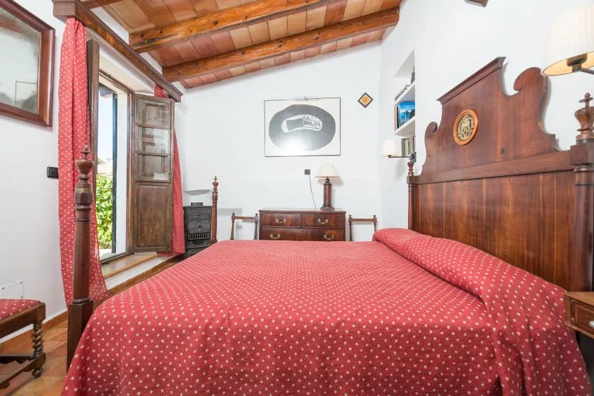 A bedroom with a red patterned bedspread and wooden furnishings.