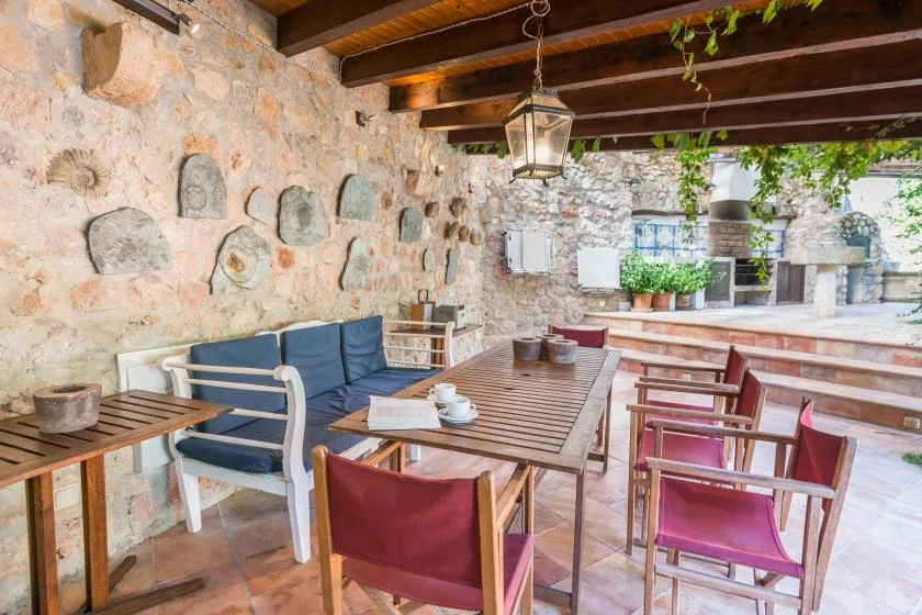Comedor exterior cubierto con mesas de madera y asientos junto a paredes de piedra.