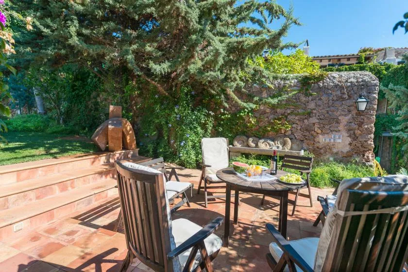 An outdoor patio with seating and a round table beneath leafy trees.
