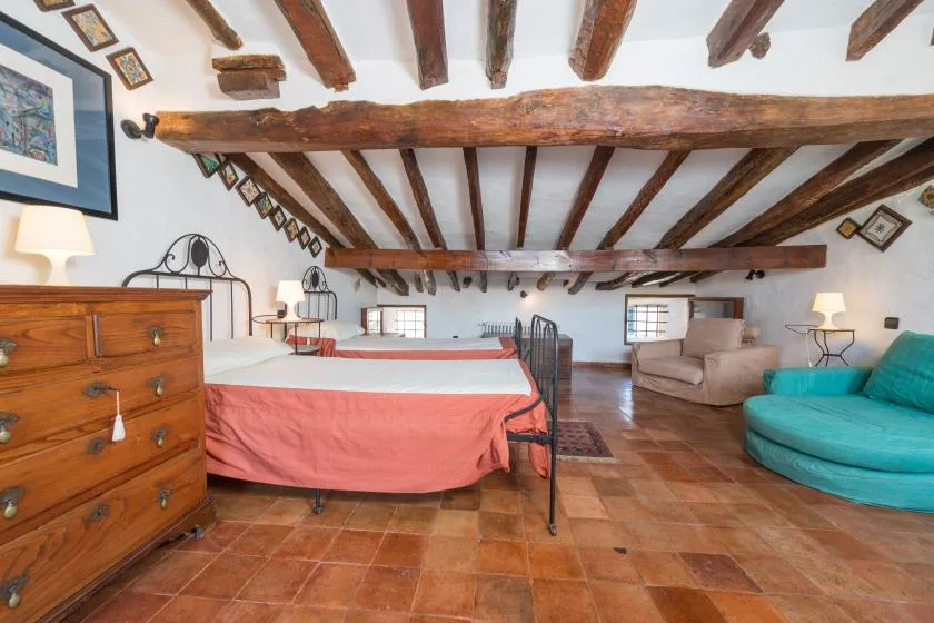 A bedroom with a bed, wooden ceiling beams, and a turquoise seating area.