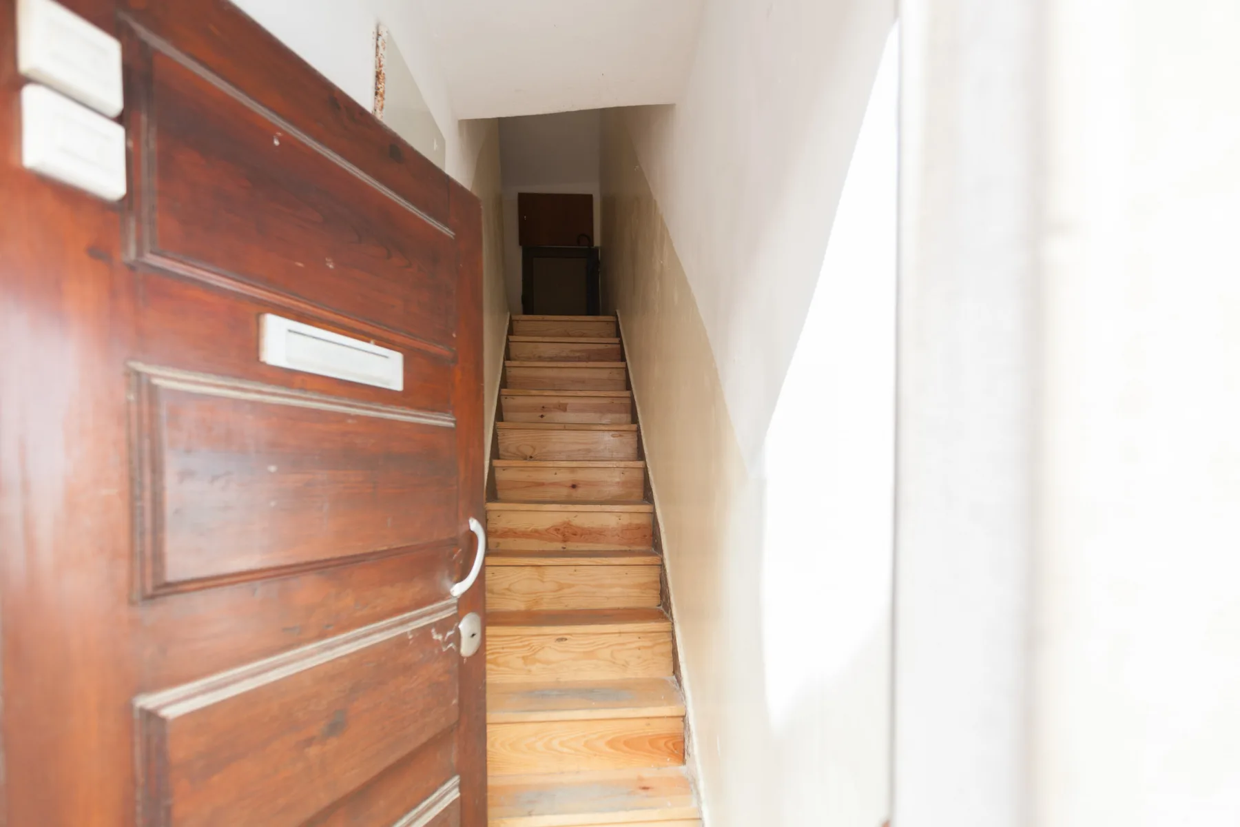 Una puerta de madera abierta deja ver una escalera estrecha que sube.