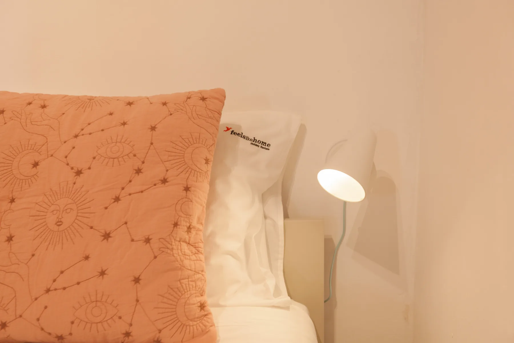 Dormitorio con un cojín estampado junto a una lámpara de noche encendida.