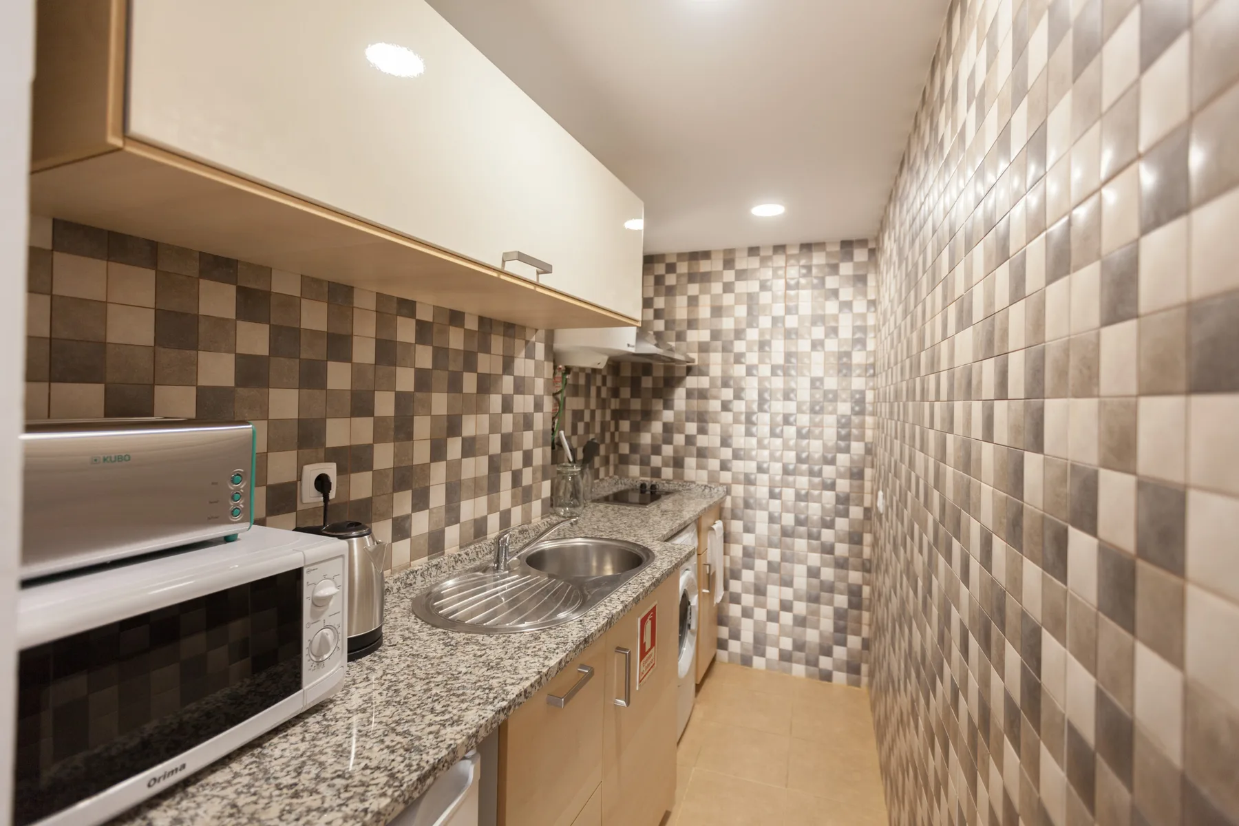 Una cocina compacta con microondas, fregadero y paredes de azulejos.