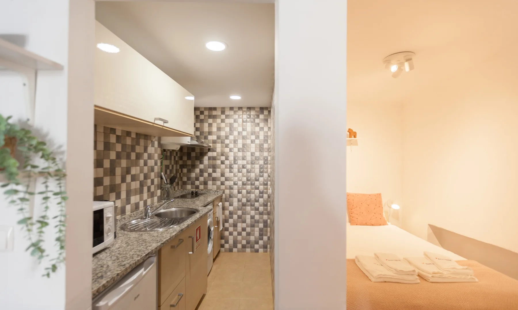 Una cocina compacta se abre junto a un dormitorio con la cama hecha.