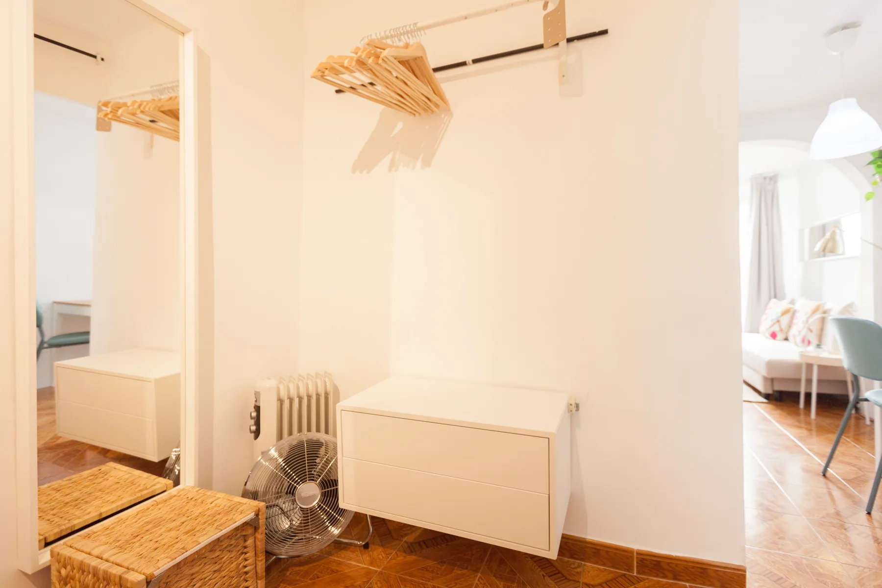 Una zona de vestidor luminosa con una barra para ropa, una cómoda y una cesta de mimbre.