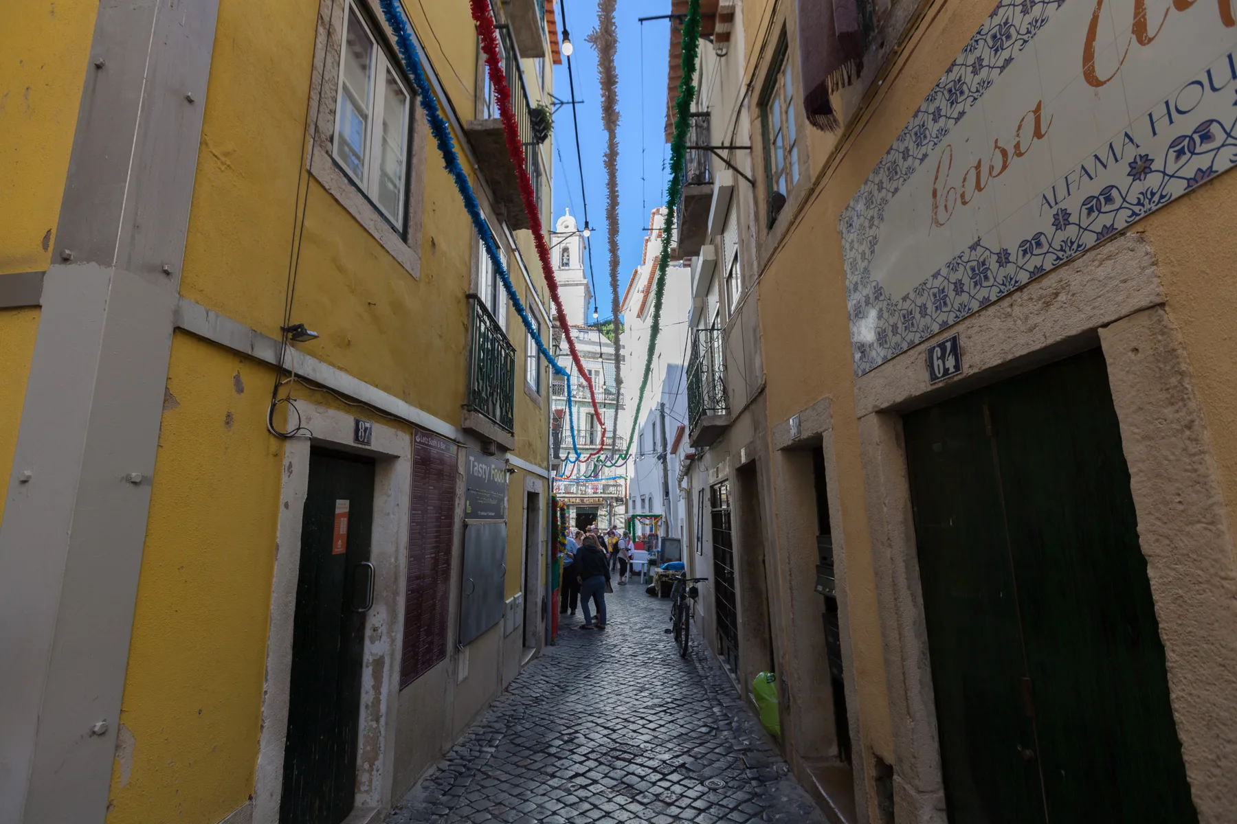 Una calle estrecha empedrada pasa entre edificios muy juntos, con peatones a lo lejos.