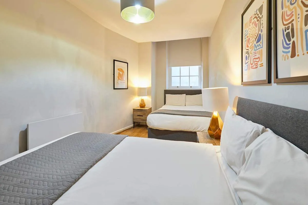 A bright bedroom with two beds and framed artwork on the walls.