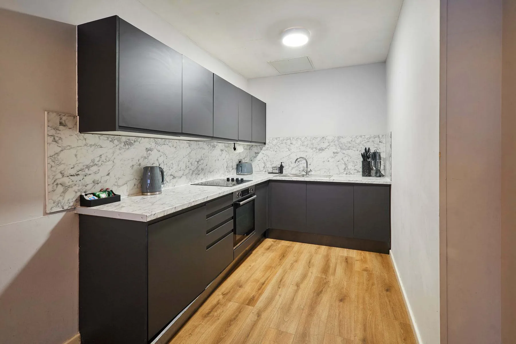 A modern kitchen with dark cabinets, light countertops, and wood flooring.