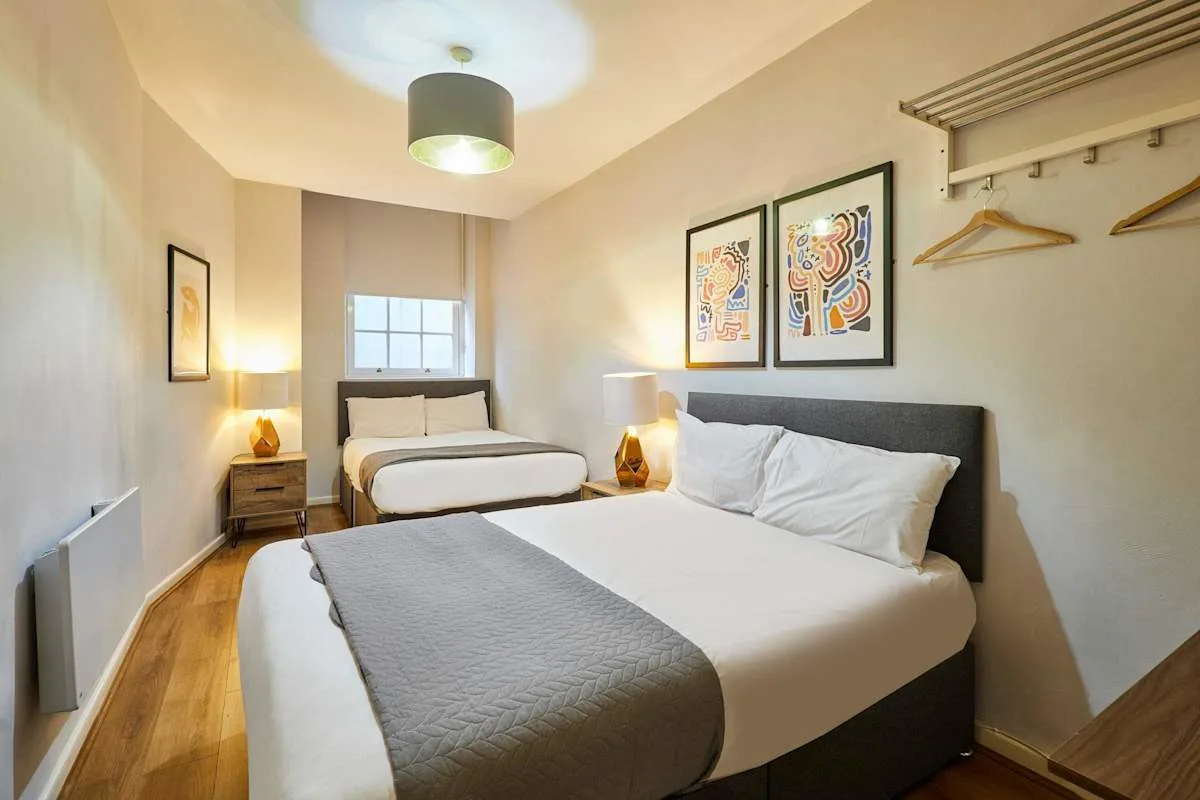 A bedroom with two beds, bedside tables, and framed artwork.