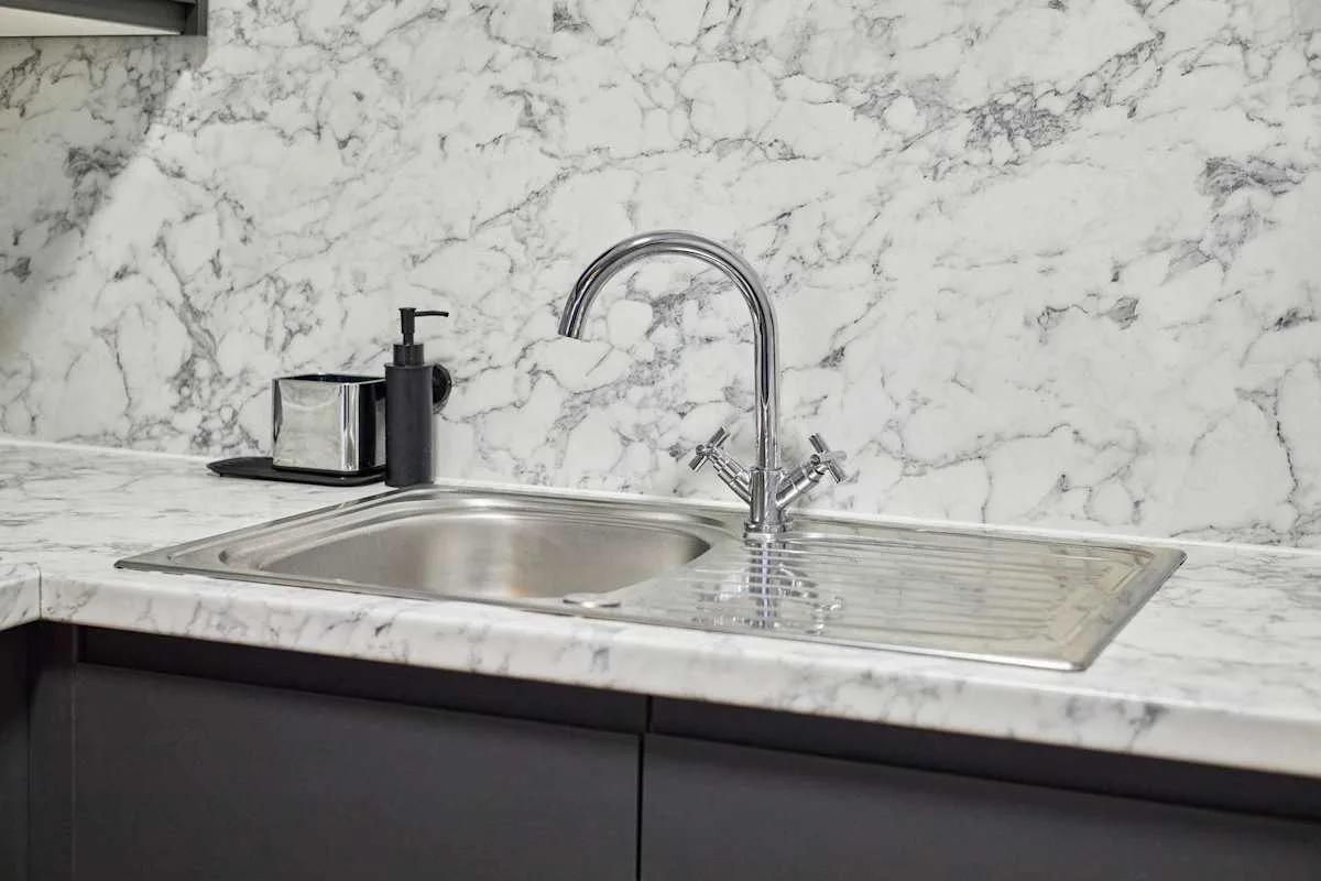 A kitchen sink and faucet are set into a light veined countertop.