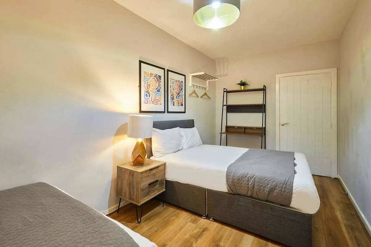 A bedroom with a neatly made bed, bedside lamp, and wall art.