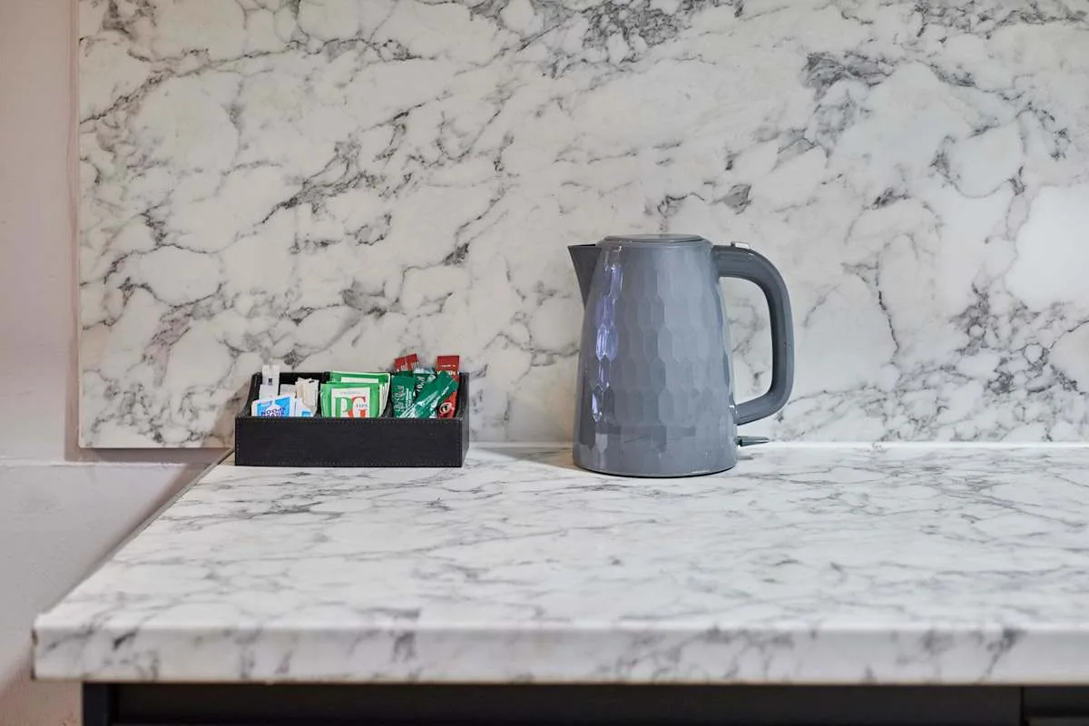 A kettle and small tray sit on a marble-patterned kitchen counter.
