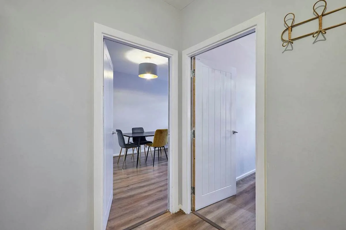 A hallway with open doorways leading to a dining area and another room.