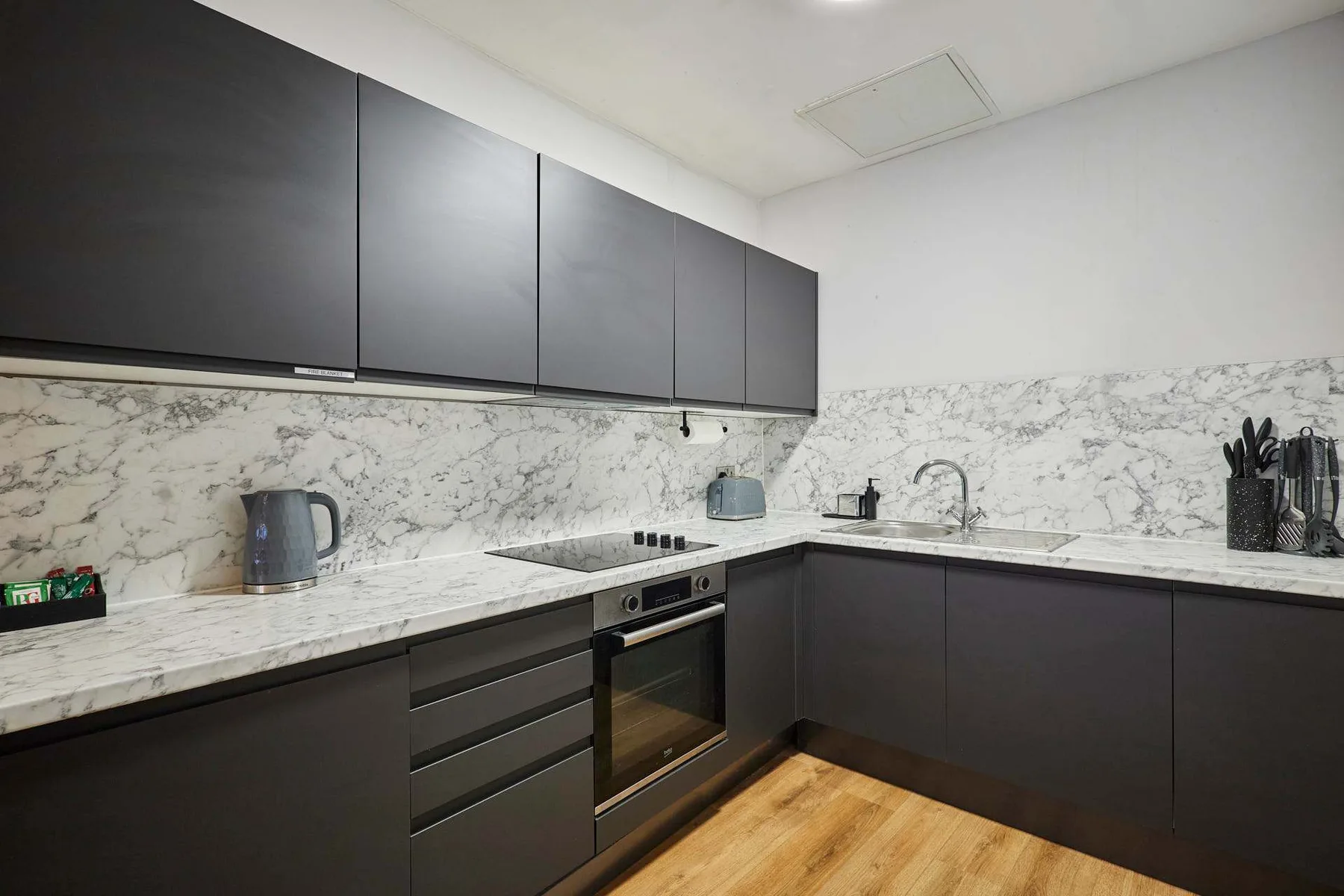 Una cocina moderna con gabinetes oscuros, encimeras con vetas y un horno integrado.