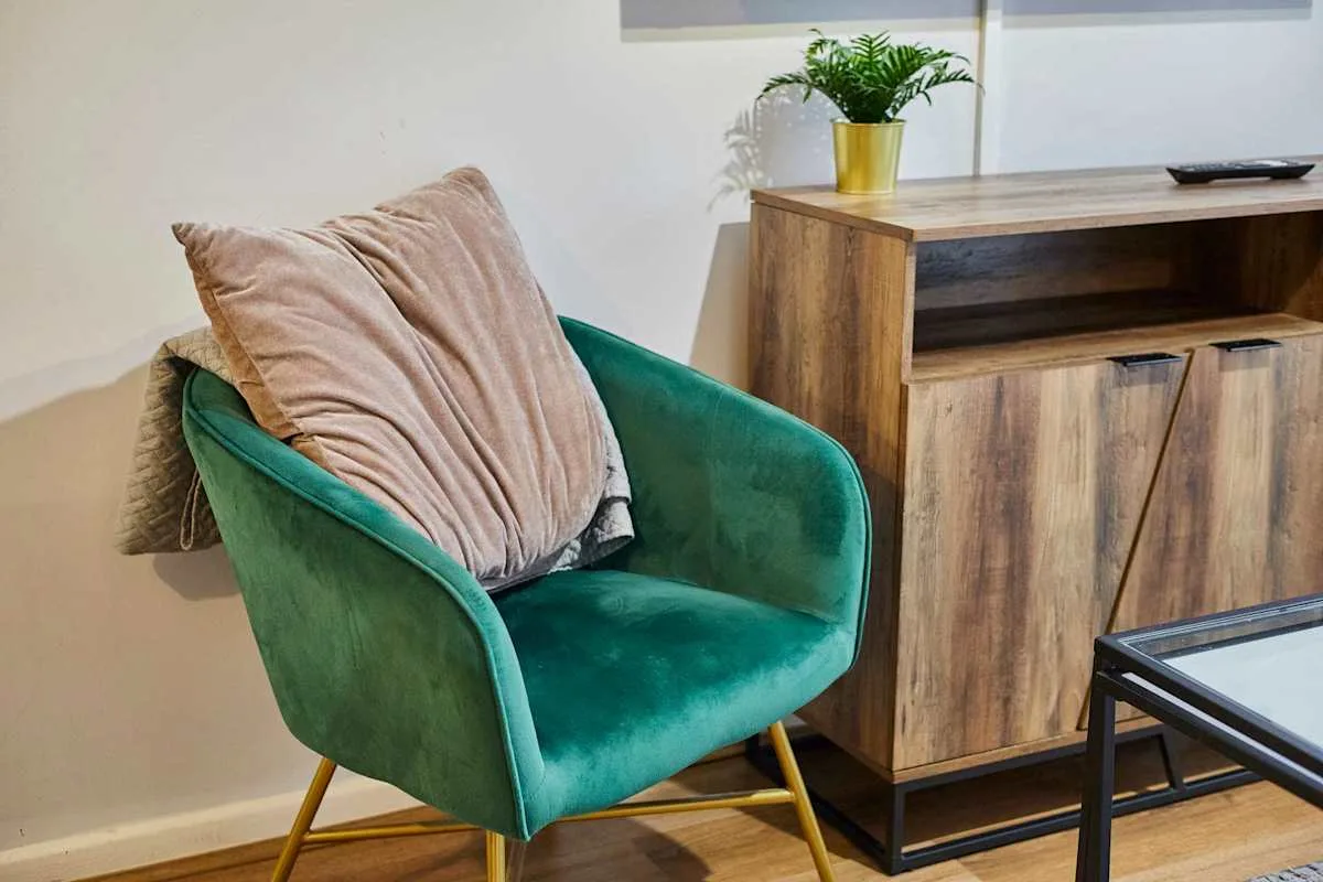 A teal upholstered armchair sits beside a wooden cabinet with a potted plant.