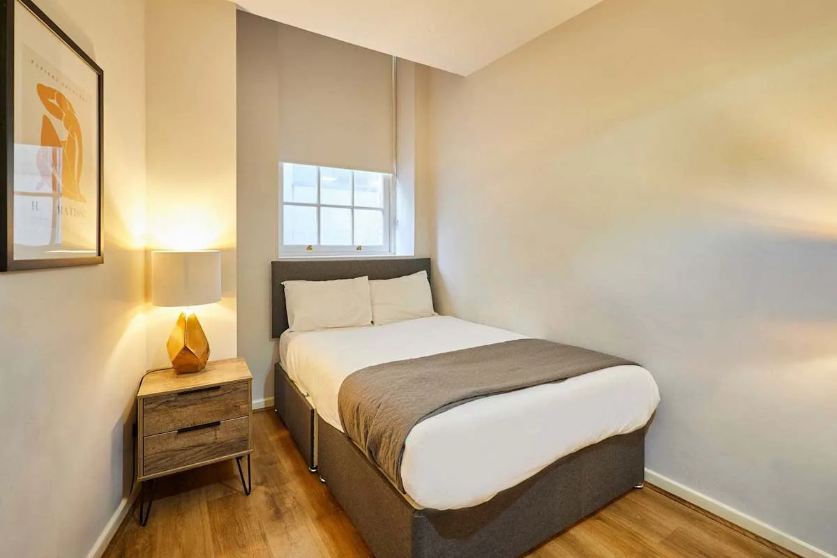 A bedroom with a neatly made bed and a window behind it.