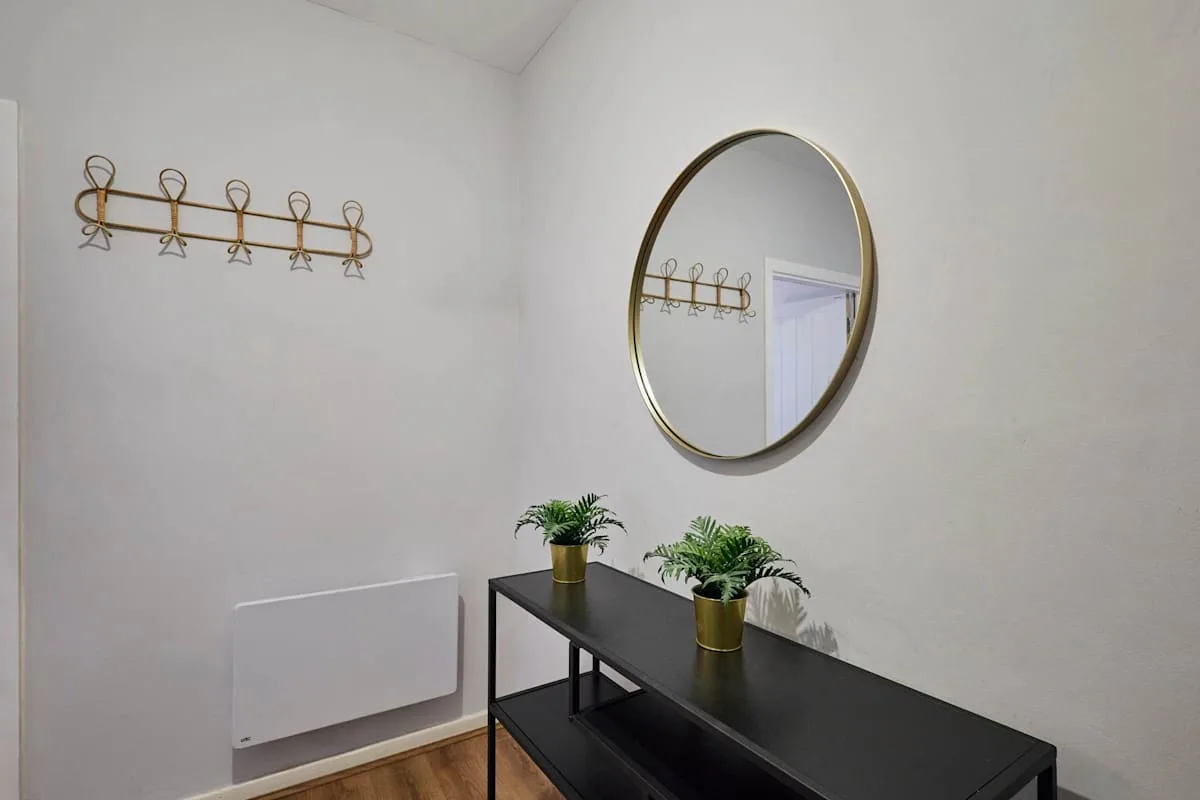 A hallway wall with a console table, round mirror, and coat hooks.