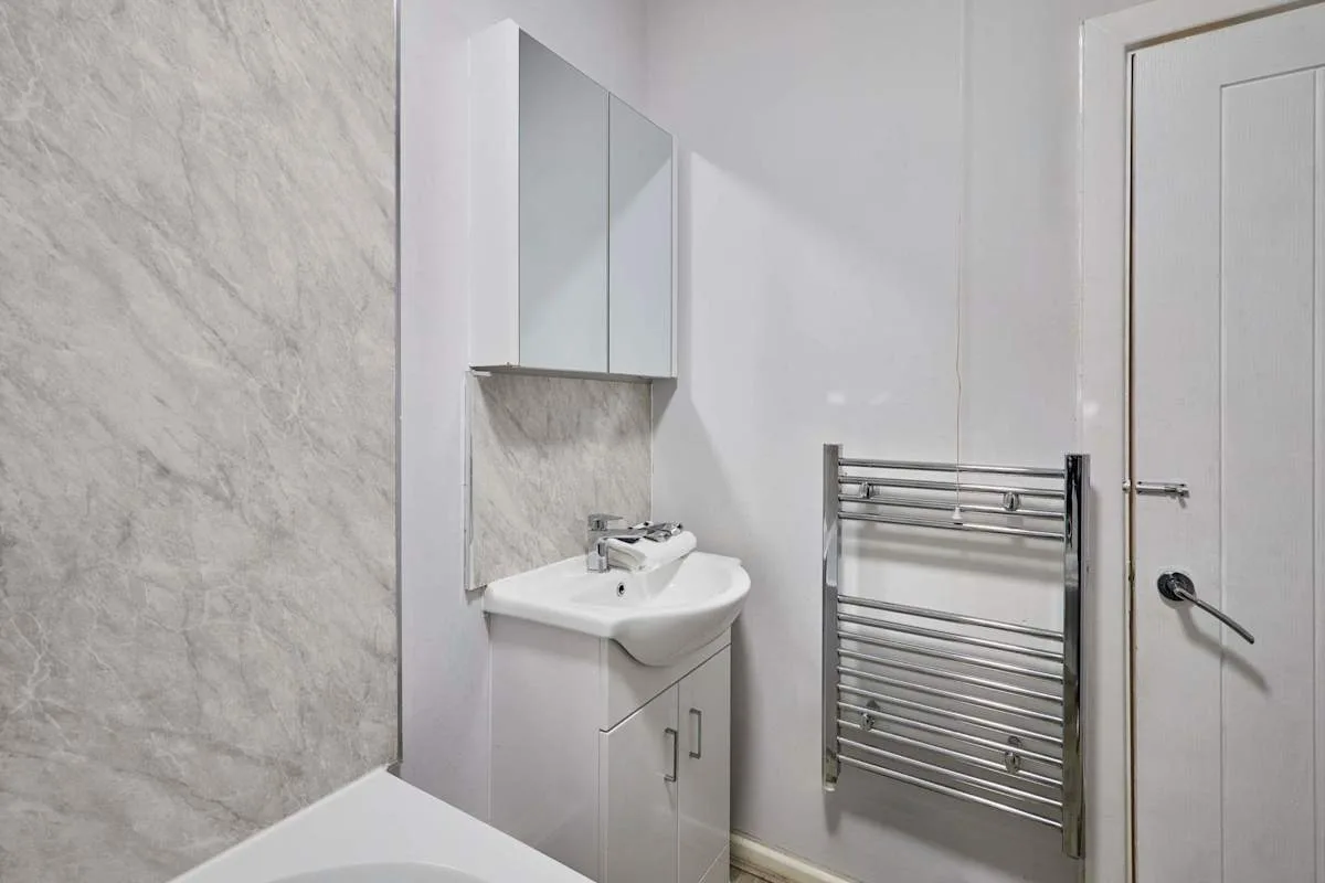 A bathroom with a sink, mirrored cabinet, towel rail, and bathtub.