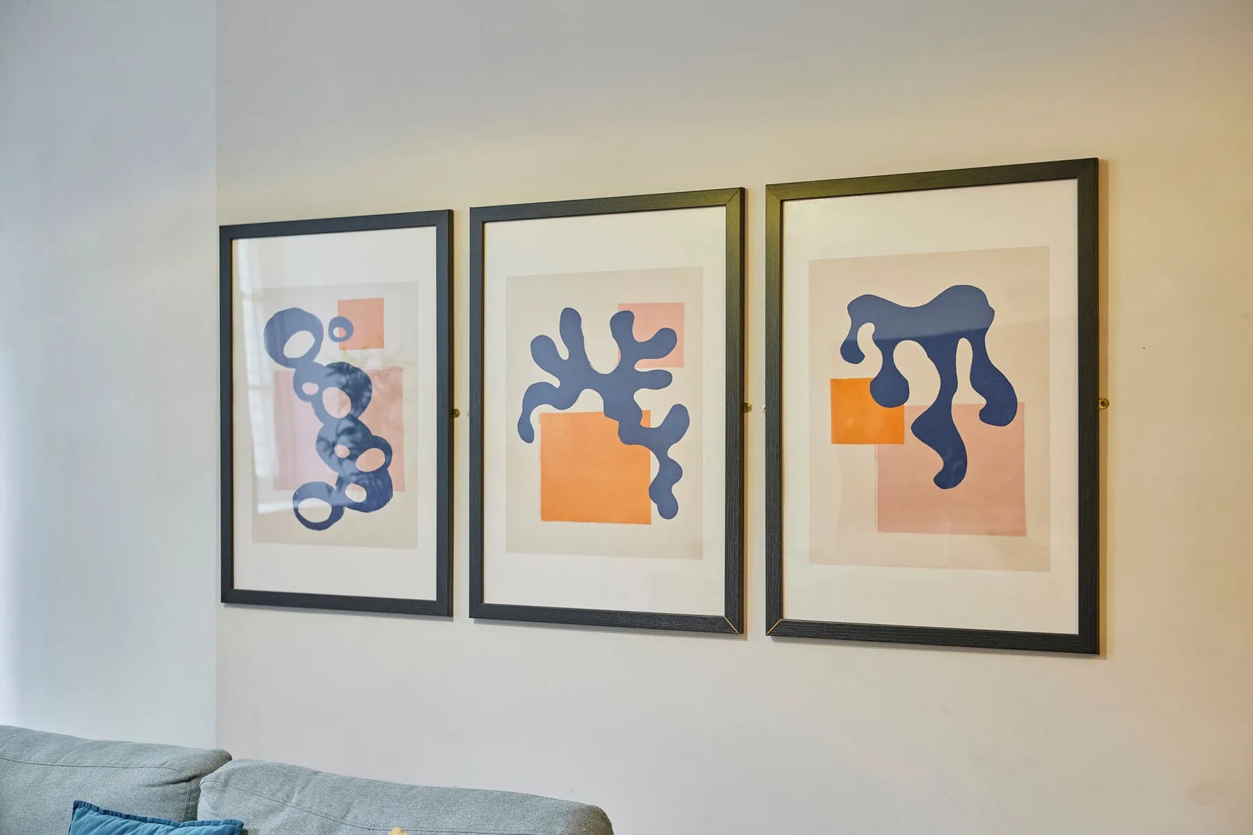 Tres láminas abstractas cuelgan sobre asientos en una escena interior sencilla.
