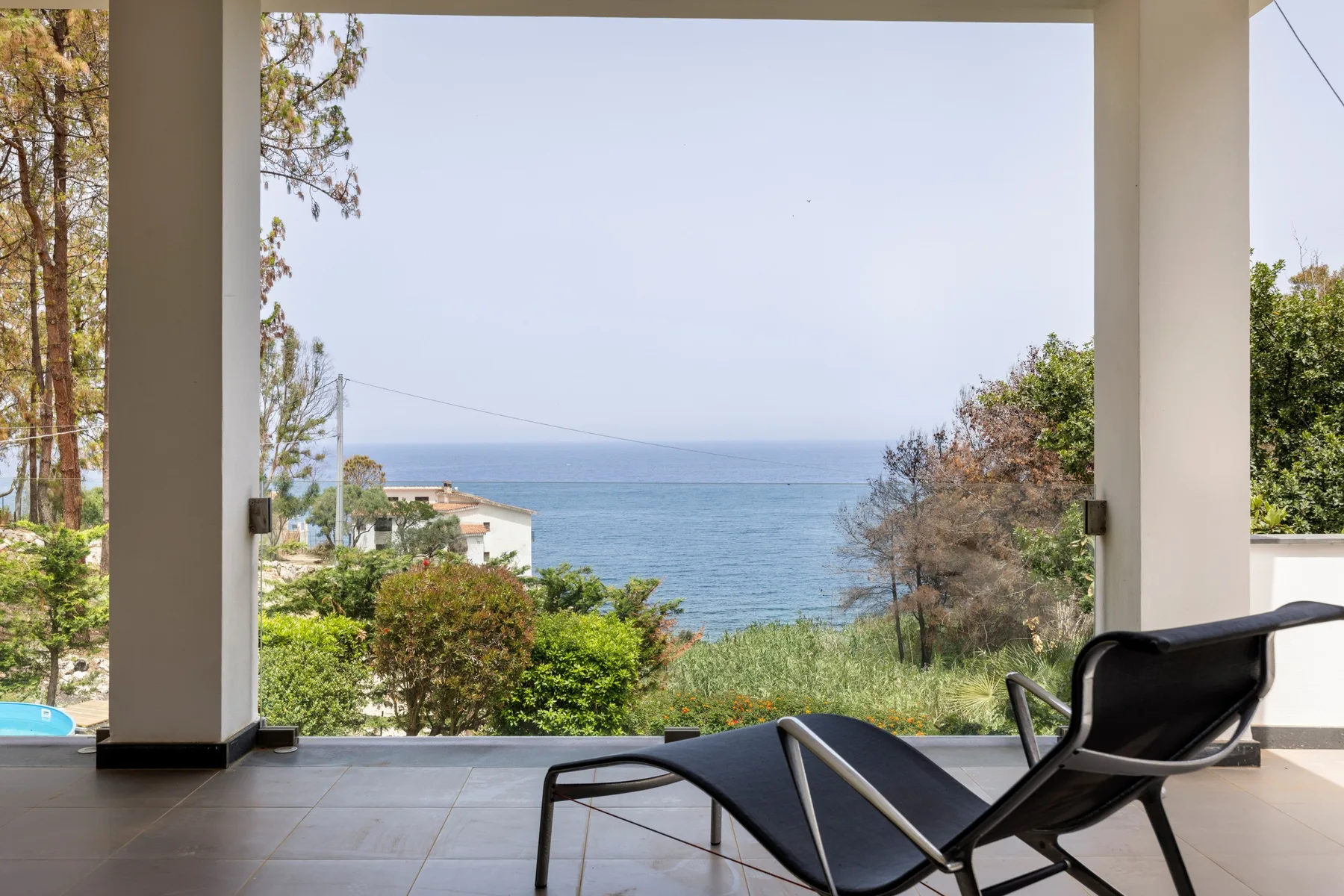 A covered terrace opens onto a sea view, with lounge seating in the foreground.