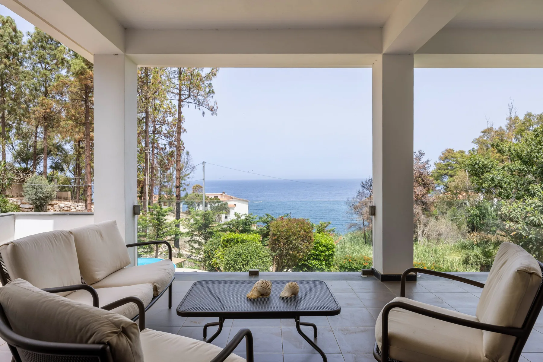 A covered patio seating area overlooks the ocean and surrounding greenery.