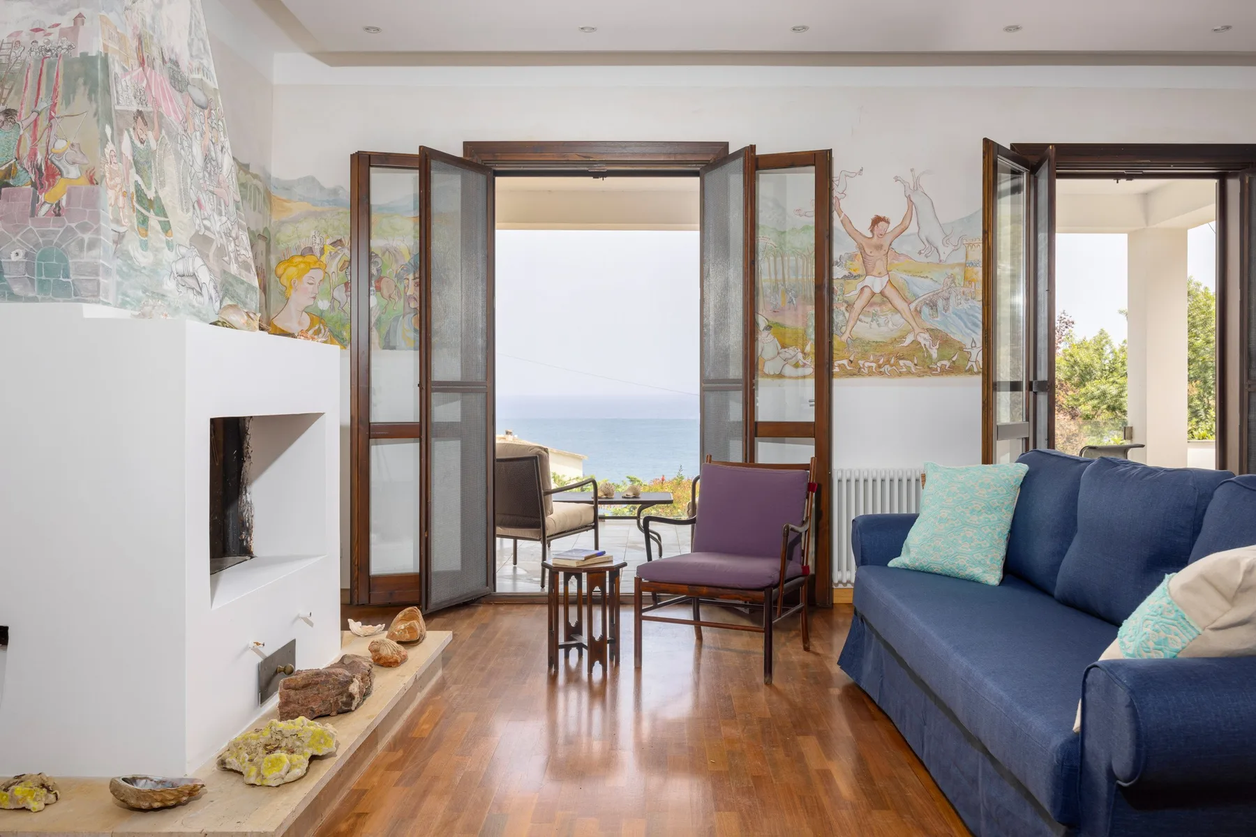 A bright living room opens onto a balcony, with seating and a fireplace.