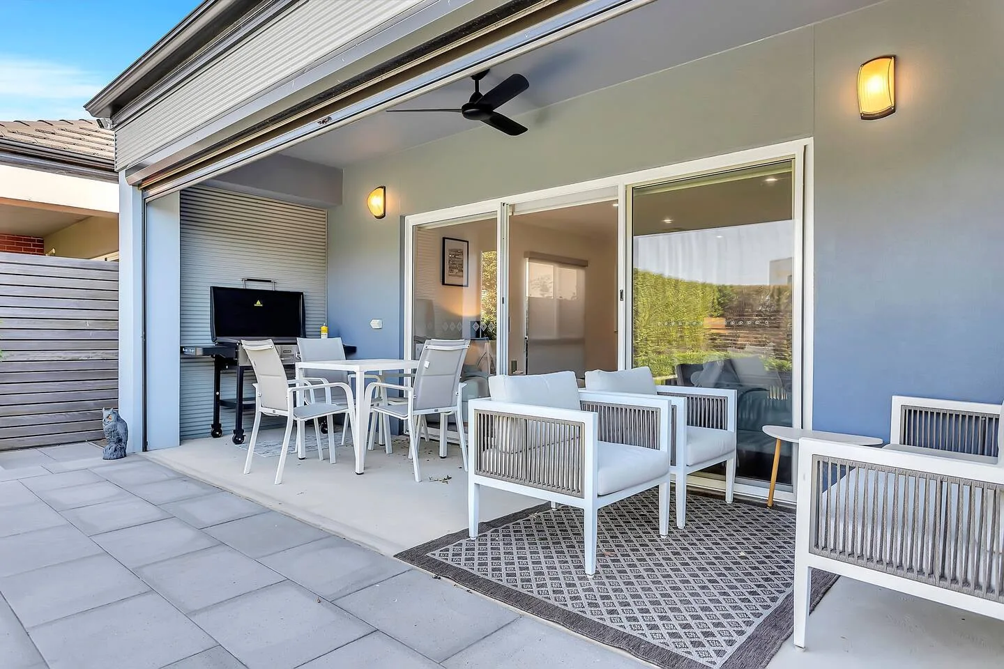 Un patio cubierto tiene asientos exteriores y una mesa de comedor junto a amplias puertas de vidrio.