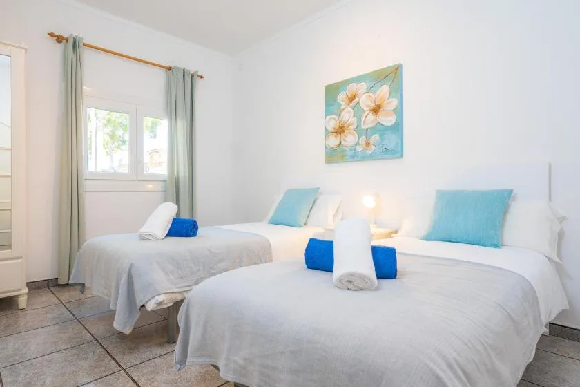 A bright bedroom with two beds, pale bedding, and a floral painting.