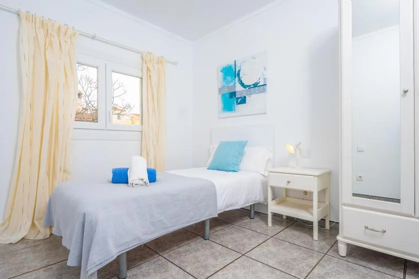 A bright bedroom with a neatly made bed and pale curtains.
