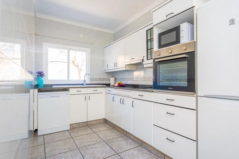 A bright kitchen with white cabinets, tiled counters, and a window.