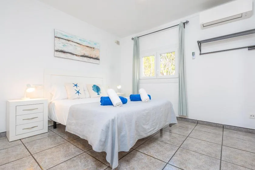 A bright bedroom with a neatly made bed and a window with pale curtains.