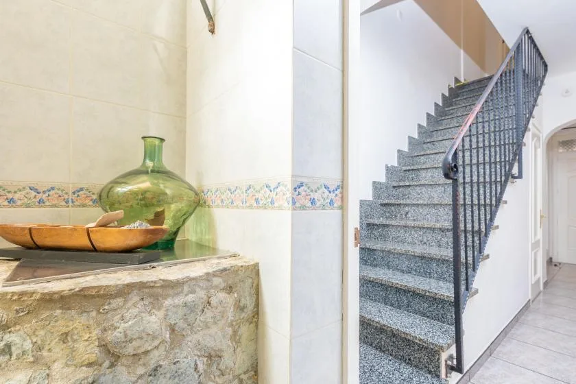 A tiled interior with a stone counter and decorative vase beside a staircase.