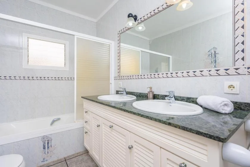 A bright bathroom features a bathtub, double sinks, and a wide mirror.