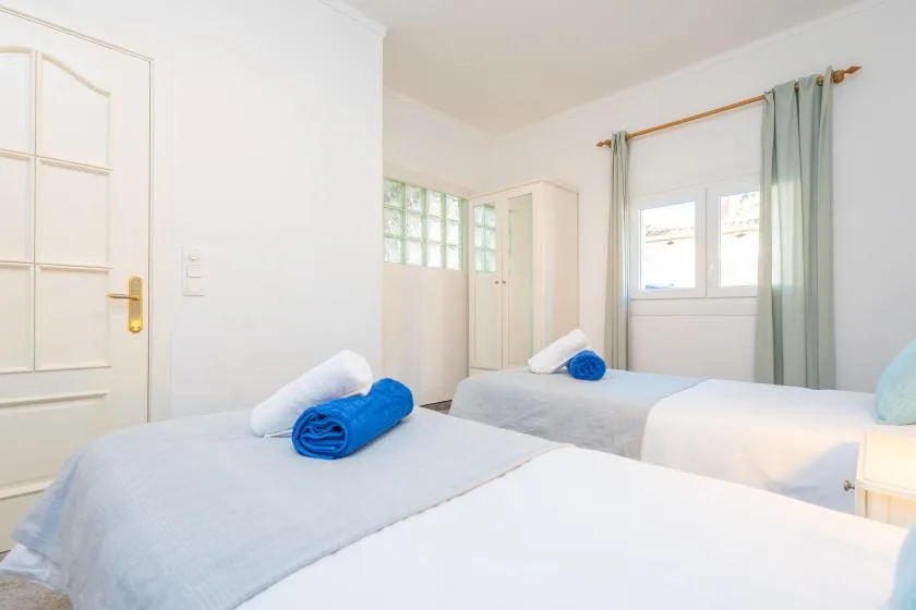A bright bedroom with two beds and folded blue towels.