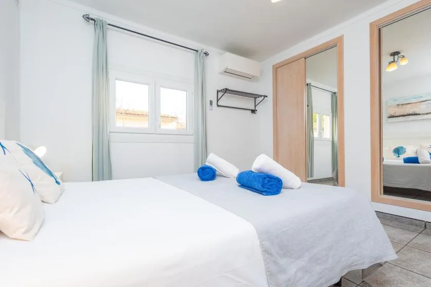 A bright bedroom with white bedding and blue towels on the bed.