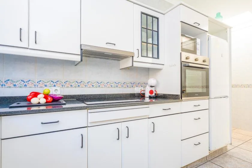 A bright kitchen with white cabinets, a dark countertop, and an oven.