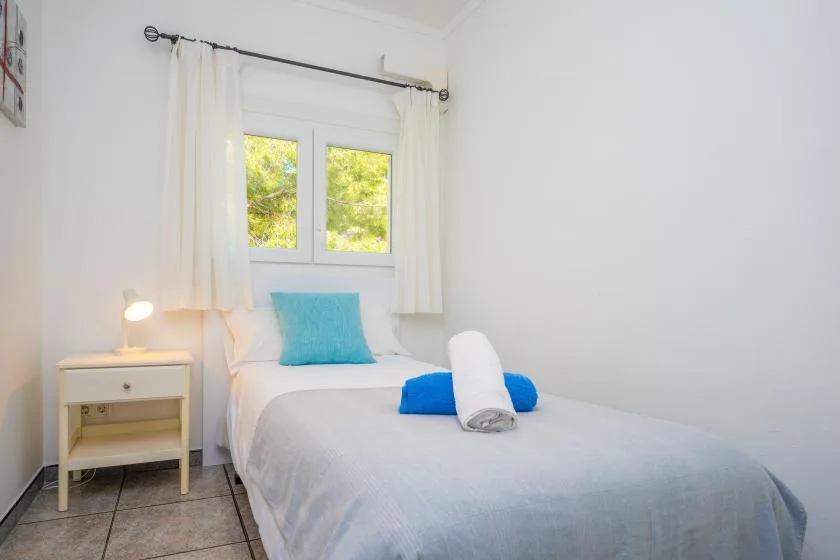 A bright bedroom with a bed beneath a window and white curtains.