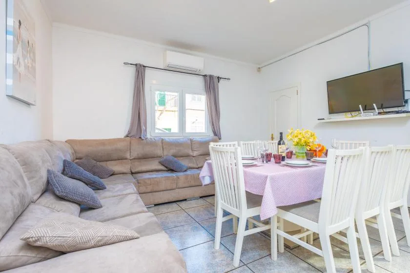 A bright living and dining area has an L-shaped seating arrangement and a set table.