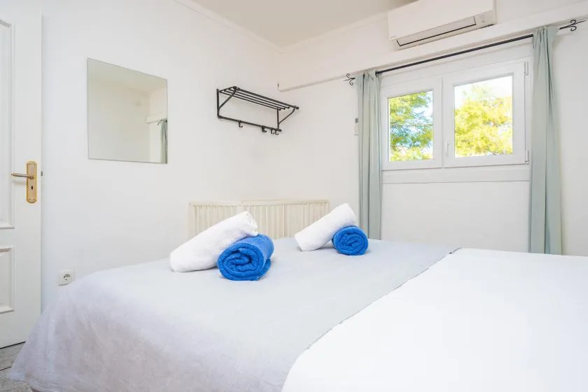 A bright bedroom with a bed, rolled towels, and a window.