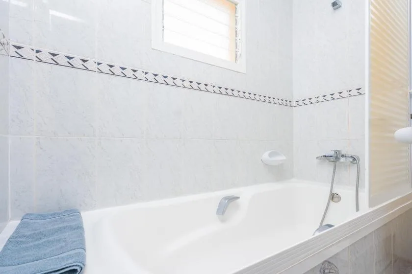 A tiled bathroom with a bathtub, wall-mounted faucet, and small window.