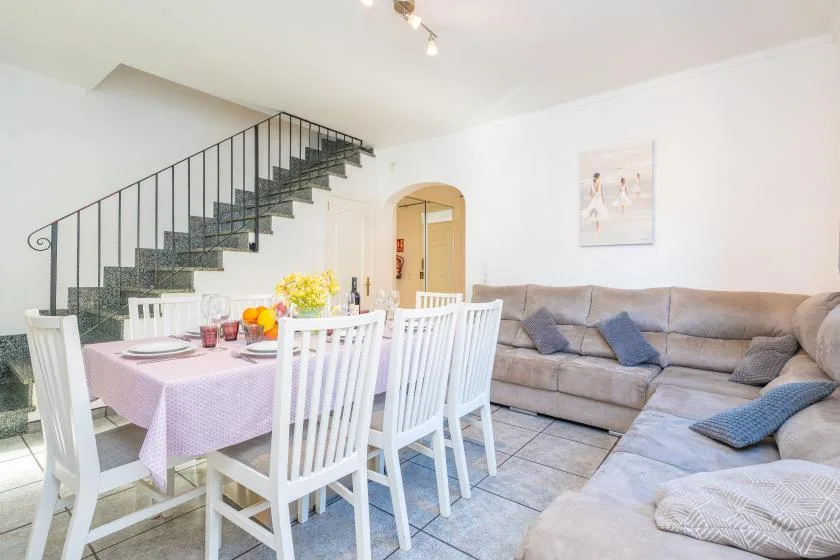 A bright living and dining area with a table, white chairs, and a sectional sofa.
