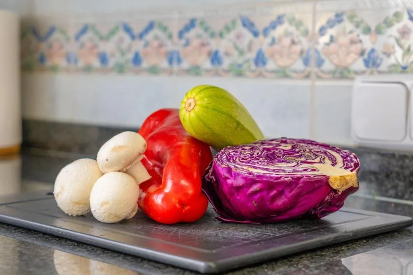 Vegetables rest on a cutting board in a tiled kitchen.
