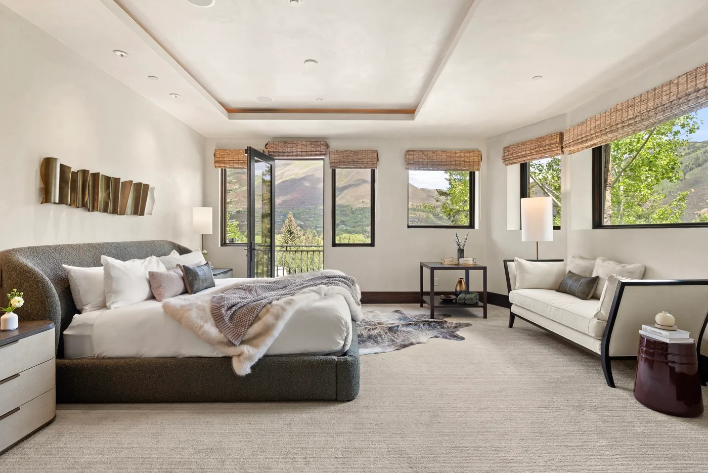 Un dormitorio luminoso con una cama grande, asientos y ventanas con vistas a la vegetación.