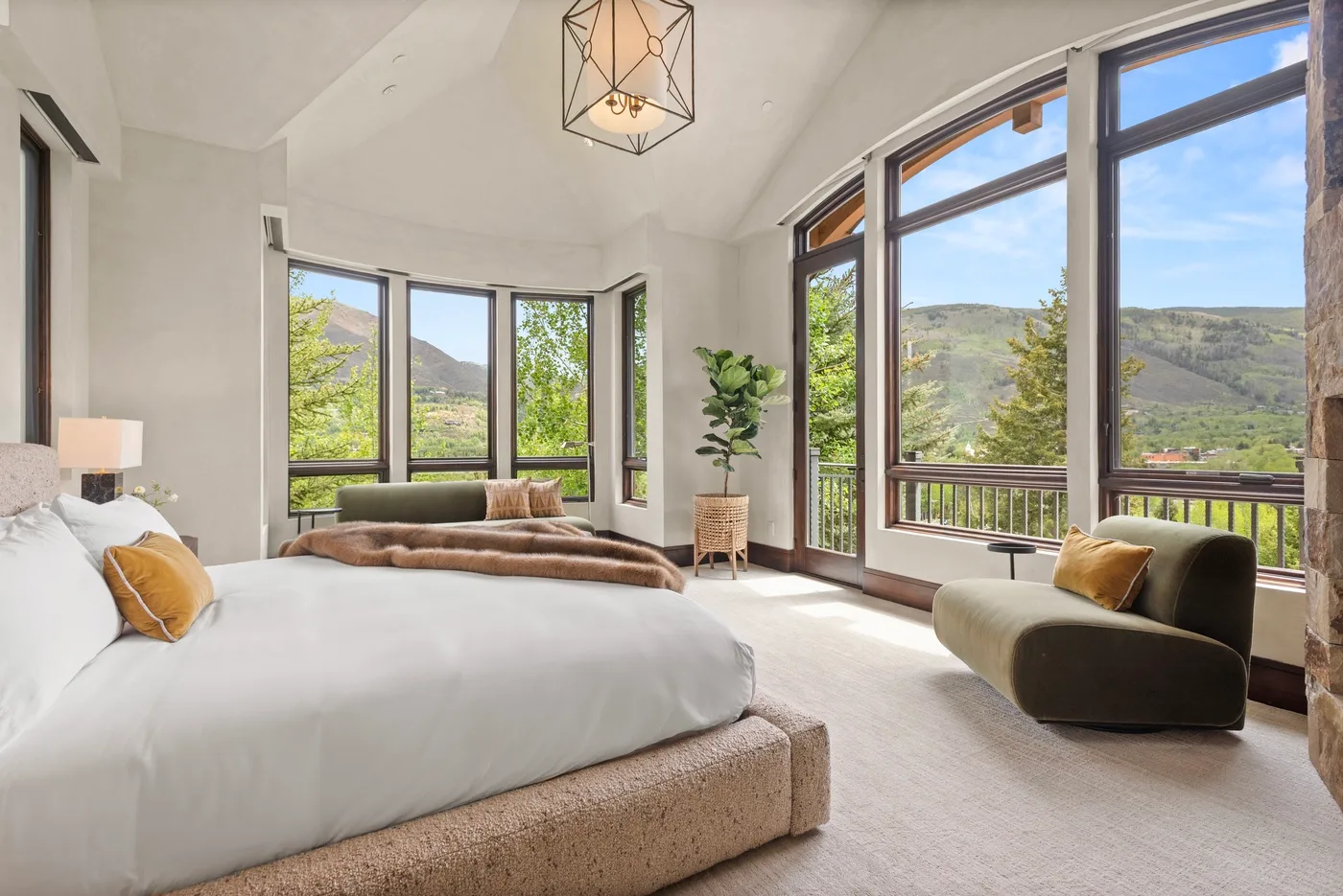 Un dormitorio luminoso con una cama grande y amplias ventanas con vistas a las colinas.