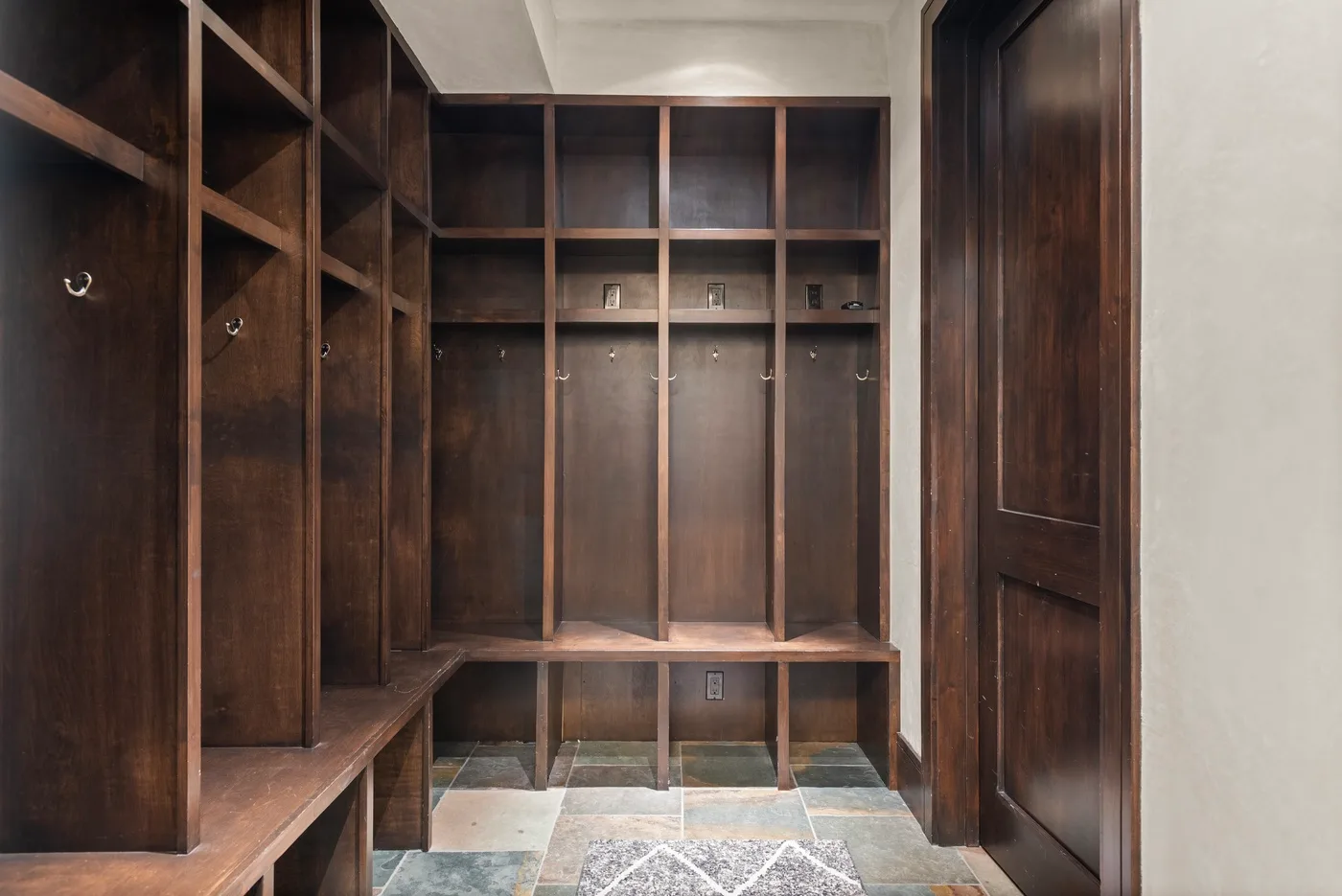 Un vestidor con estantes de madera oscura, espacio para colgar ropa y un banco.