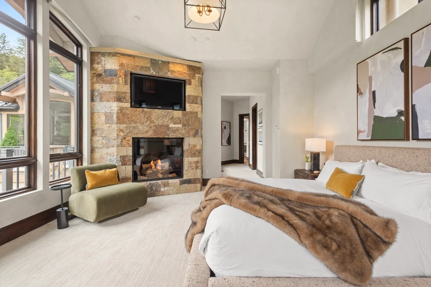 Un dormitorio luminoso con una cama, grandes ventanas y una chimenea de piedra.