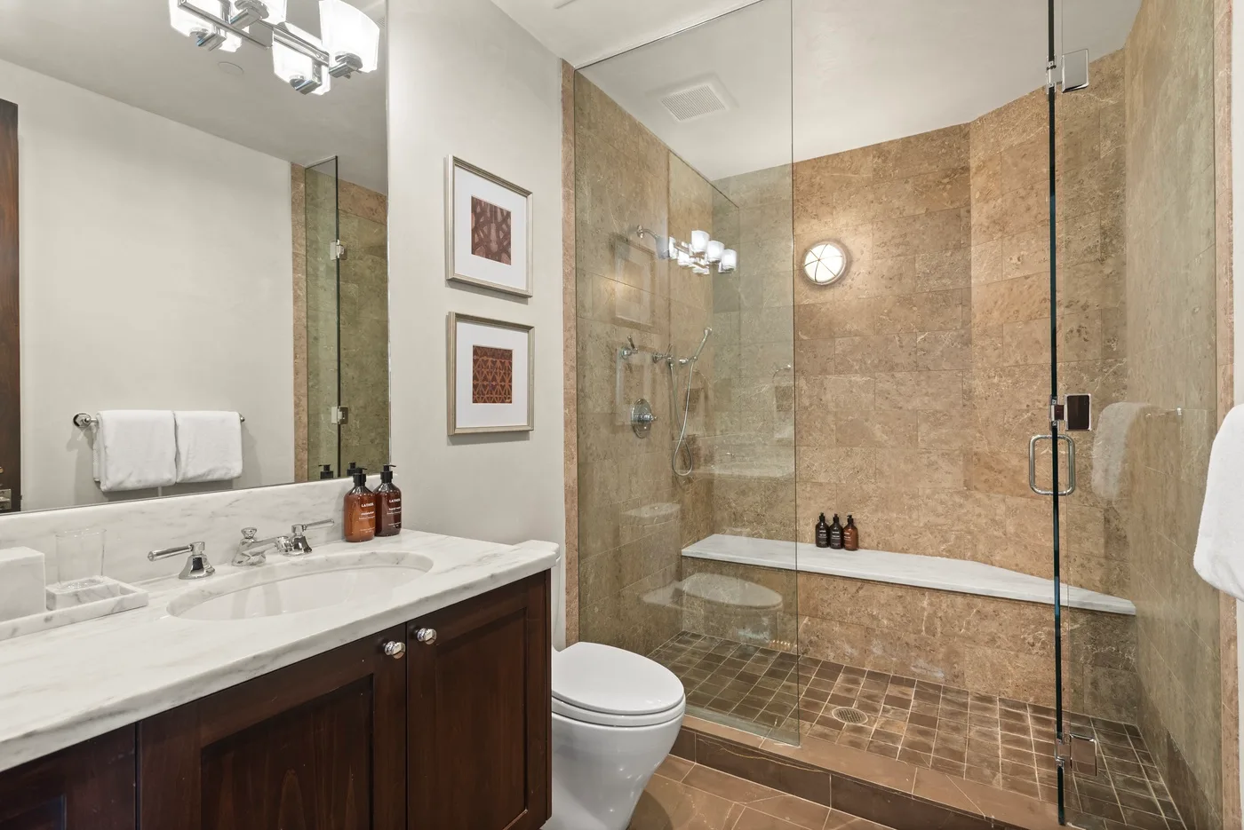 Un baño con tocador y lavabo, inodoro y ducha con mampara de vidrio.