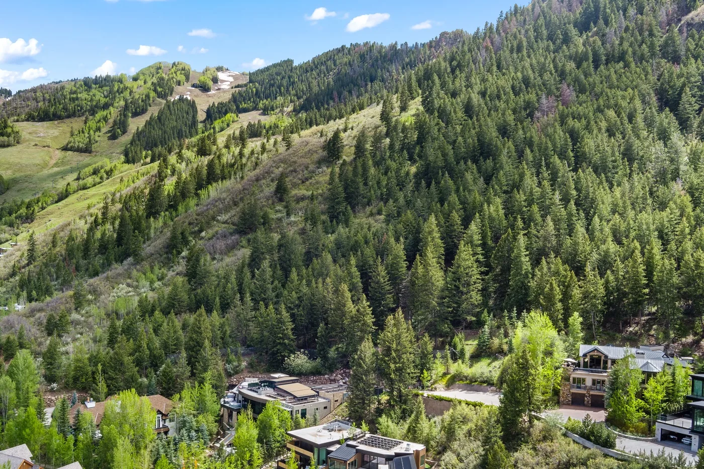 Una ladera montañosa boscosa se eleva sobre algunos edificios bajo un cielo despejado.