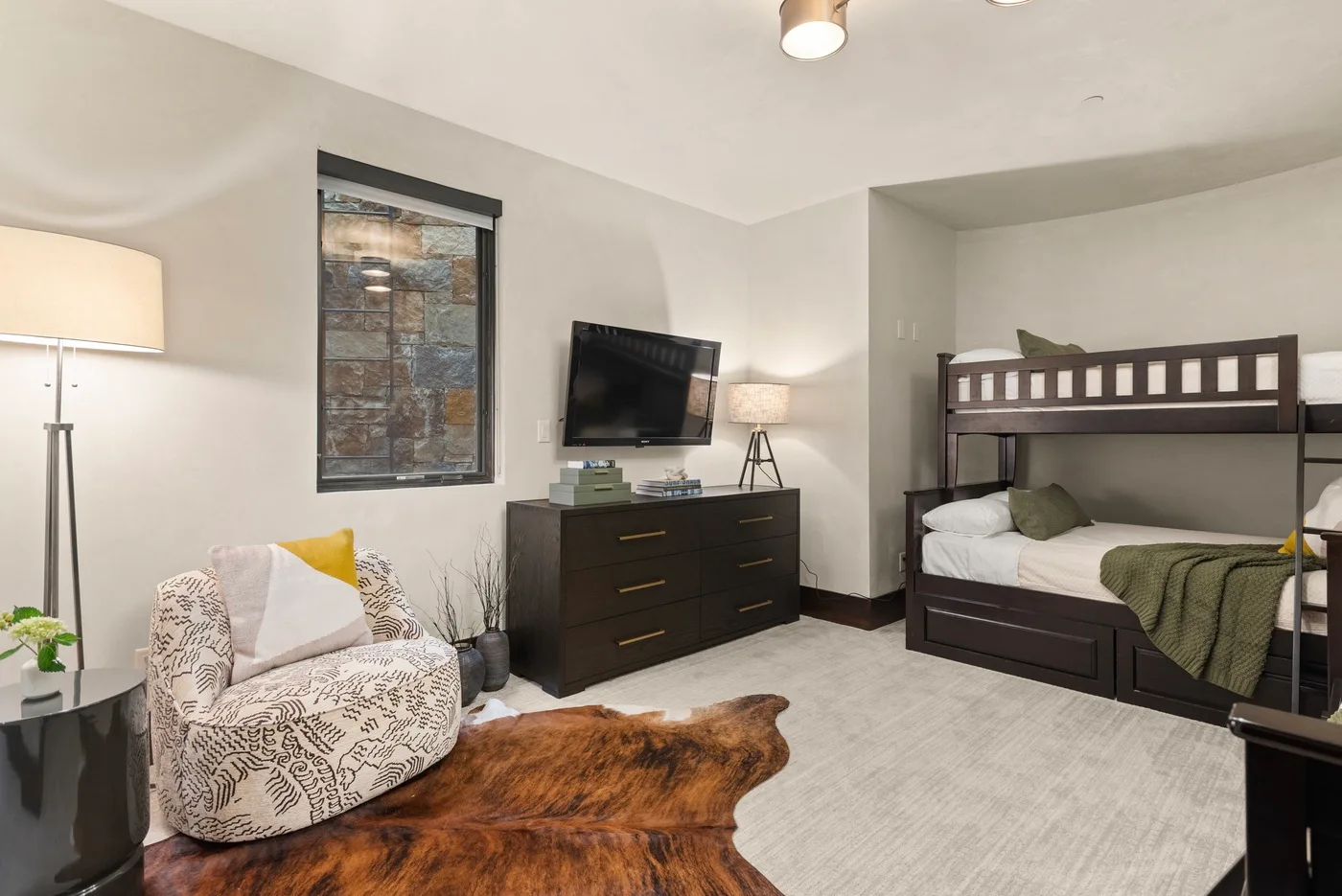Un dormitorio con literas, un televisor y un sillón estampado.